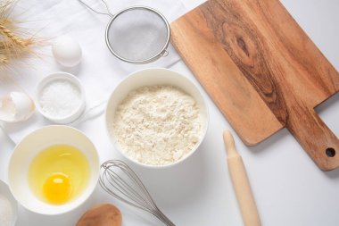 Beyaz arka planda yemek pişirmek için gerekli malzemelerin çerçevesi. Un, yumurta, şeker ve süt beyaz ve ahşap kaselerde. Pişirme ve pişirme konsepti.