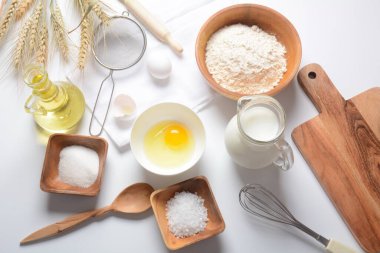 Beyaz arka planda yemek pişirmek için gerekli malzemelerin çerçevesi. Un, yumurta, şeker ve süt beyaz ve ahşap kaselerde. Pişirme ve pişirme konsepti.