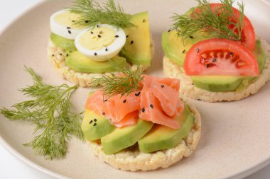 Pirinç ekmeği çıtır çıtır, avokado, haşlanmış yumurta dilimleri, somon, domates ve taze dereotu.