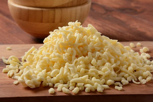 Heap of shredded cheese on small wooden board. Grated cheese for cooking on a cutting board on a wooden background