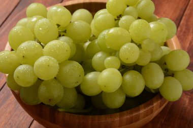 Ahşap bir kasede bir demet yeşil üzüm, sonbaharın meyveleri, kırsal ahşap arka planda