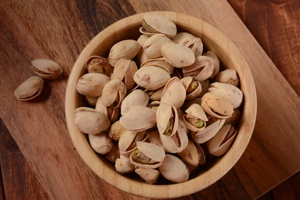 Pistachios in a wooden bowl on wooden surface, pile of pistachios, roasted pistachios in a bowl