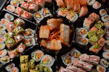 Set of sushi rolls  on a black plastic platter decorated with soy sauce and spices. Ready for delivery