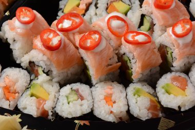Set of sushi rolls  on a black plastic platter decorated with soy sauce and spices. Ready for delivery