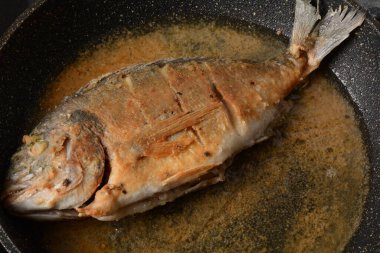 Tuz, biber ve un dolu bir tavada balık dorado pişiriyorum.