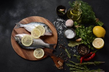 Çiğ çiğ dorado ya da limonlu, otlu, yağlı, sebzeli ve baharatlı çipuralı balık siyah arka planda kırsal ahşap tahtada.