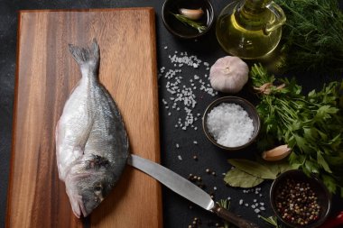 Çiğ çiğ dorado ya da limonlu, otlu, yağlı, sebzeli ve baharatlı çipuralı balık siyah arka planda kırsal ahşap tahtada.