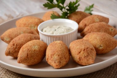 Deep fried kibbeh of ground beef meat mixed with bulgur, stuffed with fried minced meat with pine nuts on a clay plate on wooden table