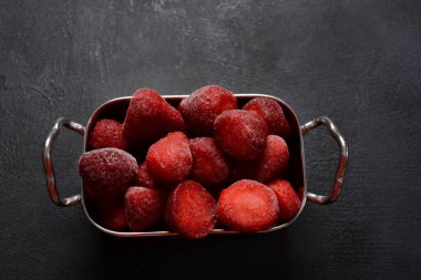 Koyu arkaplanda gümüş kasede donmuş çilekler.