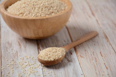 Eski ahşap arka planda beyaz susam tohumlu ahşap kase ve kaşık.