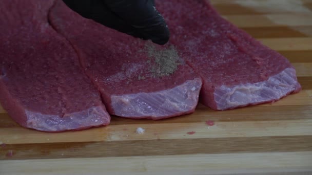 Mann Schwarzen Handschuhen Gibt Sanft Pfeffer Auf Die Rohen Fleischscheiben — Stockvideo