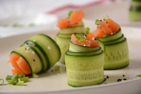 Cucumber rolls with pieces of salted salmon, black and white sesame seeds, chopped green onion. Holiday vegetable appetizers