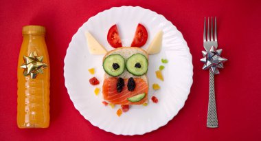 Kızarmış ekmek, kırmızı balık, peynir, sebze üzümü ve meyve suyundan yapılmış yenilebilir 2021 boğa ineği sembollü komik bir sandviç. Çocuklar için kahvaltı fikri. Noel yemeği üst görünümü. yemek sanatı