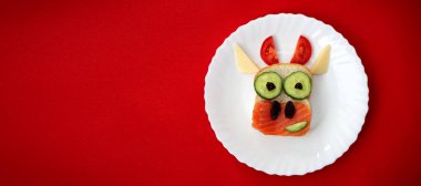 Yenebilir 2021 boğa ineği sembollü komik sandviç kızarmış ekmek, kırmızı balık, salatalık, domates, peynir ve kuru üzümden yapılır. Çocuklar için kahvaltı fikri. Noel yemeği üst görünümü. Yemek sanatı.