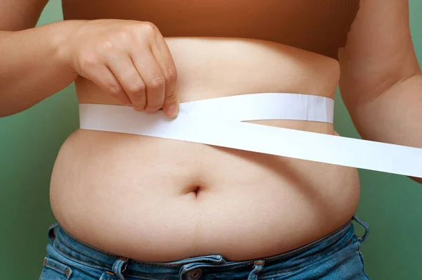 Overweight fat woman measuring her belly fat with measuring tape close up
