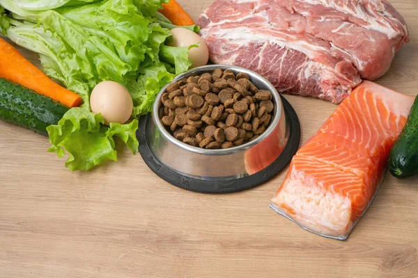 天然成分を使用したドライペットドッグフード 生の肉 サラダをボウルの近くに置き 木製の背景に乾いたペットの餌を与えます ペットのための正しいバランスの取れた栄養という概念は — ストック写真