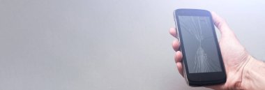 Gri arka planda kırık ekranlı cep telefonu. Kopyalama alanı olan pankart