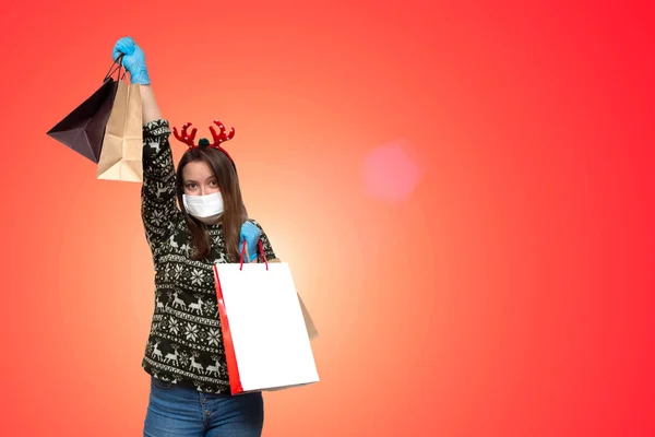 白い医療マスクと手にギフトパッケージとクリスマスの赤い帽子の若いヨーロッパの女性 クリスマスショッピングガールXmasの隔離コロナウイルス — ストック写真