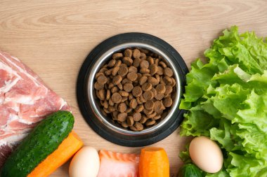 Doğal malzemeli kurutulmuş köpek maması. Çiğ et, balık, sebze, yumurta ve salatanın yanında ahşap arka planda kuru hayvan yemi. Evcil hayvan için doğru dengeli beslenme kavramı, düz