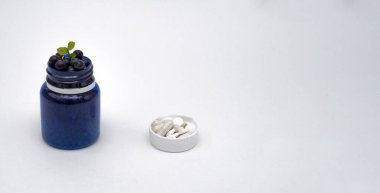 İçinde vitamin böğürtlen hapları olan mavi şişe. kopyalama alanı olan beyaz arkaplan