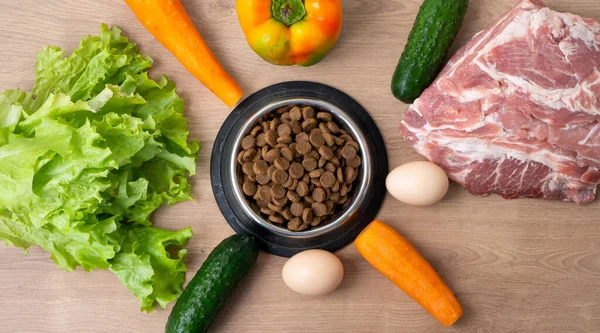 天然成分を使用したドライペットドッグフード 生の肉 サラダを木製の背景に乾いたペットの餌でボウルの近くに ペットのための正しいバランスのとれた健康的な栄養という概念は — ストック写真
