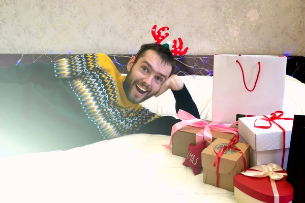 ベッドの上で弓とクリスマスや新年のギフトボックス 鹿の角の男は贈り物の山の近くにある クリスマスの挨拶 — ストック写真
