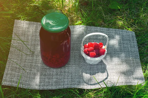 Raspberry drink in jar and ripe raspberry outside on green leaf and sunlight background