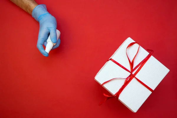 Mão em luvas médicas desinfetando uma caixa de presente festivo coronavírus prevenção — Fotografia de Stock