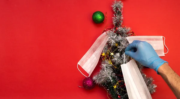 La mano en guantes médicos decora el árbol de Navidad con máscaras médicas. El concepto de celebrar el año nuevo y la Navidad bajo restricciones de coronavirus. vacaciones en cuarentena — Foto de Stock