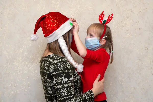 Família, mãe e filha em máscaras protetoras em quarentena nas férias de Natal em chapéu de santa klaus e chifres profundos. Vida normal com coronavírus. Estilo de vida COVID-19. Protecção de quarentena. — Fotografia de Stock