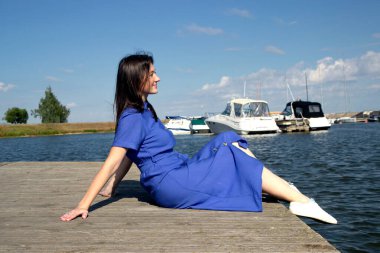 Arka planda rıhtımda oturan rüya gören kız ve nehir manzarası. Sakin sakin kadın gölün kıyısında dinleniyor, güneşin ve güzel havanın tadını çıkarıyor.