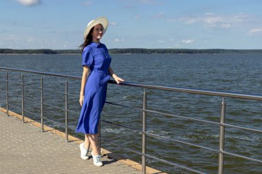 İskelede saman şapkalı, zarif elbiseli genç bir kadın harika bir manzaranın tadını çıkarıyor..