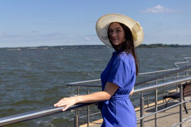 İskelede saman şapkalı, zarif elbiseli genç bir kadın harika bir manzaranın tadını çıkarıyor..