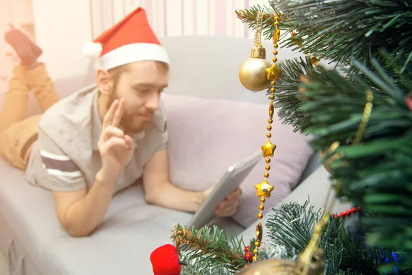 クリスマスオンラインおめでとうございます ビデオ通話の友人や両親のためにタブレットを使用してクリスマスツリーの近くに笑顔男 家にいて社会的孤立選択的焦点を当て — ストック写真