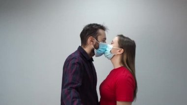 Koruyucu maskeli genç bir çift ellerinde tuttukları kırmızı kağıt kalbi öpüyor ve örtüyor. Sevgililer Günü 'nü 2021' de kutlayın. Coronavirüs karantina konsepti.