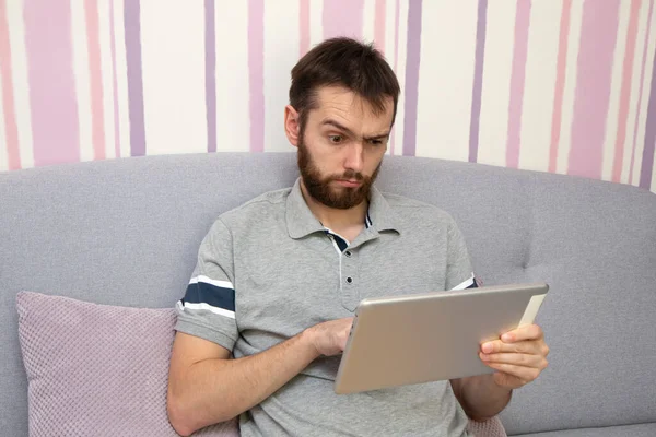 Atractivo Joven Con Barba Está Utilizando Una Tableta Sorprendido Sofá —  Fotos de Stock