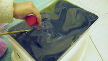 Babası olan çocuk su yüzeyinde boya ve fırçayla mermer desenler yapıyor. Ebru sanatı