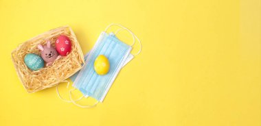 Paskalya Düzlüğü tıbbi bir maskeyle yatıyordu. Renkli boyanmış yumurtalar beyaz tepside samanlıkta yatıyordu. Covid-19 salgını ve karantinası sırasında tatil kavramı. Kopyalama alanı ile yerleşim