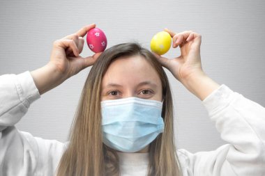 Paskalya yumurtaları ile üzgün genç bir kadın koruyucu tıbbi maske takıyor..