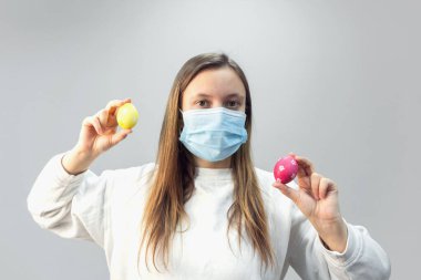 Paskalya yumurtaları ile üzgün genç bir kadın koruyucu tıbbi maske takıyor..