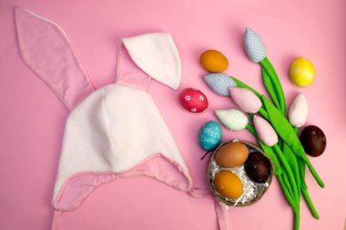 Paskalya arkaplanı boyalı yumurtalar, renkli laleler ve kulaklı Paskalya tavşanı şapkası. düz kart