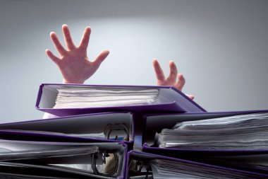 Ofis masasındaki yüzük klasörlerinin arkasına batan birinin elini kaldırdı. Aşırı talepler ve iş hayatında artan çalışma kavramı. seçili odak