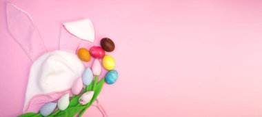 Paskalya arkaplanı boyalı yumurtalar, renkli laleler ve kulaklı Paskalya tavşanı şapkası. Fotokopi alanı olan düz pankart