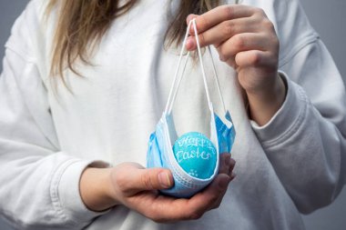 Paskalya yumurtalarını tıbbi bir maskenin içinde tutan eller. Coronavirus salgını sırasındaki Paskalya sembolü. Paskalya 2021 'de karantinada güvenlik