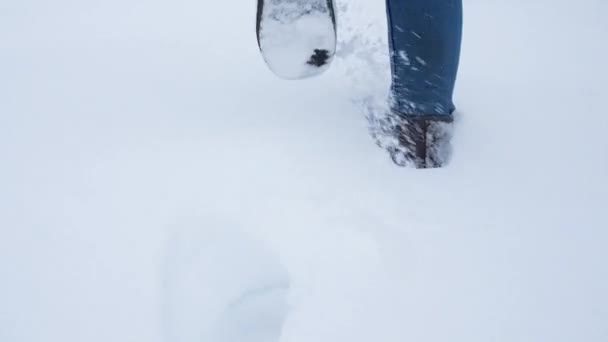 Benen går på snö med fotspår. Bakifrån. kameran följer benen — Stockvideo
