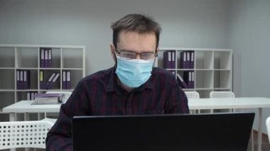 Koruyucu tıbbi maske taktığı için gözlük buğulanmış. Salgın sırasında ofiste çalışan bir adam. İçeride maske takmakta zorlanıyorum.