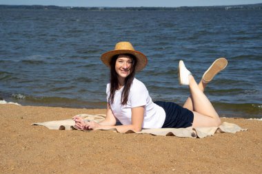 Temiz hava soluyan rahat bir kadının yan görüntüsü, parlak sıcak güneşin altında kumların üzerinde uzanan deniz ve gökyüzü arka planda.