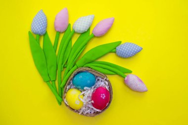Yuvasında boyanmış yumurtalar ve renkli laleler olan Paskalya kartı. Üst görünüm ve düz sarı arkaplan.