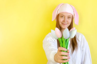 Paskalya tavşanı kulaklı kadın, sarı arka planda, üzerinde fotokopi alanı olan bahar laleleri uzatıyor.