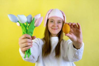 Paskalya tavşanı kulaklı kadın, sarı arka planda, üzerinde fotokopi alanı olan bahar laleleri çiçek ve yumurta uzatıyor.